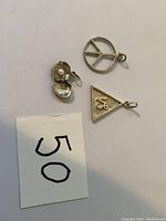 Three silver pendants including a peace sign, triangular pendant, and open shell with pearl visible.