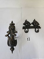 Photo showing the brass door knocker with an ornate design next to the cast iron pony double hook hanger with two hooks, against a white background with a number 13 label.