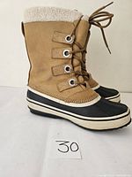 Side angle view of the caramel-colored Wind River boots with black lower soles and white faux-shearling lining visible at the top cuff. Lace-up front detail.