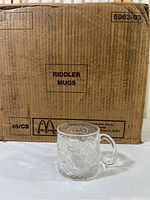 Box labeled 'Riddler Mugs' with quantity 48 indicated, cardboard box with McDonald's branding and date stamp Apr 23 95.