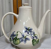 Front angle view of white ceramic teapot with blue floral hand-painted design and handle