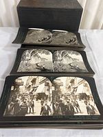 Stack of vintage Keystone stereoscopic slides showing black and white double images, with a dark box behind them.