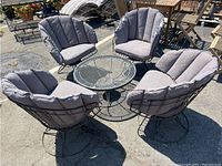 Full set of one metal mesh round table and four matching swivel chairs with grey cushions displayed outside.