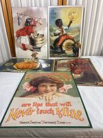 Five vintage metal signs displayed against a white table and corrugated wall, showing various subjects including children, Native American figure, and advertising slogans.