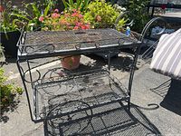 Side angle view of the black wrought iron serving/plant cart showing two mesh shelves and decorative scroll sides.