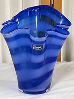 Front view of a ruffled edge blue and white striped glass vase with Alicja label.