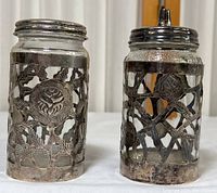Two vintage silver plated jars side by side showing the intricate openwork designs, lids, and some tarnishing
