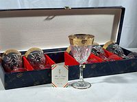 Set of six crystal wine glasses in original blue box with gold floral design and red velvet inserts. One glass displayed upright showing gold rim detail.