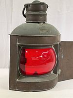 Front view of the antique brass lantern showing rounded red glass panel and open door.