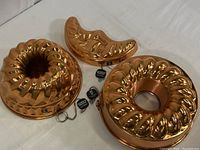 Set of three copper baking pans including two Bundt pans and one boot-shaped mold on white background.