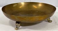 Full side view of the brass bowl showing its round shape and three ornate feet.