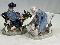 Two Royal Copenhagen farm figurines of a boy and girl with cows, side by side