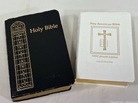 Front view of two Bibles together: black Holy Bible and white New American Bible.