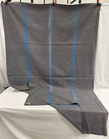 Full view of the grey wool camp blanket with two vertical navy blue stripes, draped for display showing overall pattern and fabric condition.