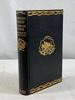 Front angled view of vintage book 'Tristram Shandy' by Lawrence Sterne showing black cover with gold embossed decorative border and central illustration.