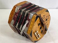 Image shows the entire wooden-panel wooden octagonal body of the accordion with metal reinforcements, white buttons, and one worn leather strap visible.