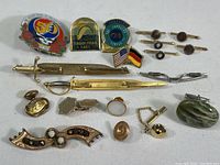 Full view of lot contents including swords tie clips, cufflinks, pins, and brooch with assorted colors and metals.