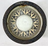 Front view showing compass face with directional markings and rim inscription '10 51 07'. Glass cracked near center.