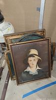 Five vintage framed art pieces stacked, front piece portrait of child wearing hat