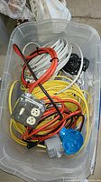 Plastic bin filled with assorted electric cables and two metal electrical outlet boxes, one with a blue cap cover.