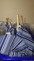 Two cushioned hammocks with blue and white stripes hanging together, showing wooden spreader bars and ropes.