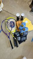 Overview of various sports equipment including three tennis rackets, baseball mitt, boxing gloves, swim flippers, and tubes of badminton shuttlecocks