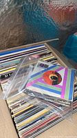 Box of assorted vinyl records including 7" singles in plastic sleeves and LPs visible