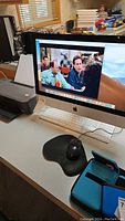 Apple iMac displaying sitcom scene on screen, showing entire all-in-one computer with keyboard and mouse.