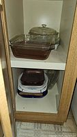 Two shelves inside a cabinet holding multiple pieces of glass bakeware including various rectangular and round dishes, some with lids