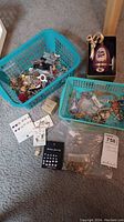 The overall assortment of costume jewelry in two teal plastic baskets, multiple small plastic bags with jewelry pieces, and the decorative egg-shaped ornament boxed
