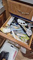 Photo showing an open drawer full of various kitchen utensils and tools including spatulas, scissors, pasta tool, wooden spoon, whisk, and more.