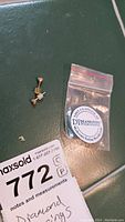 Photo of the pair of diamond stud earrings and a small plastic bag with Diamonds International sticker, also showing the MaxSold lot tag.