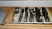 Drawer with trays holding various types of flatware including forks, spoons, and knives.
