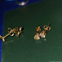 Close-up image showing two pairs of gold stud earrings on a green surface.