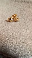 Two small gold stud earrings with faceted rounded tops and screw back posts on beige fabric