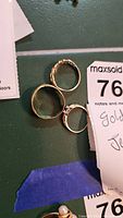 Three gold rings arranged on green surface with MaxSold tag