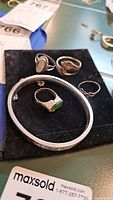 Photo of four silver rings and one silver bracelet on black velvet pouch with MaxSold tag visible.