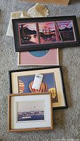 Four framed artworks displayed on the floor including nautical triptych, hot air balloon print, cityscape photo, and another framed art.