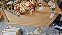 Photo showing light wood trunk with various decorative items placed on top, including a large polka dot clown doll and small figurines.