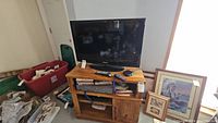 Samsung 32-inch flat screen TV on wooden TV stand with remotes and other items.