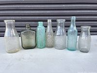View of seven varied glass bottles lined up in front of grey roll-up door
