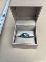Sterling silver ring with blue opal stone inlays inside a beige jewelry box, shown with a measuring tape beside it for scale.