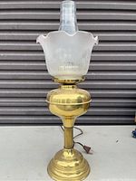 Front view of brass electric lamp resembling an oil lamp, showing polished brass body and frosted glass shade with floral etching
