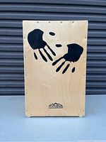 Front view of the Mountain Rhythm cajon drum showing black handprint design on a light wood front panel.