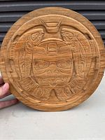 Close-up of the round cedar wood lid with detailed hand carved indigenous design including stylized animal shapes and geometric patterns.