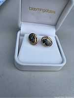 Close-up photo of two oval gold plated cuff links with centrally set patterned stones in a white Bloomingdale's jewelry box.