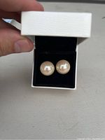Close-up photo of a pair of large pearl earrings in a white box with black velvet interior.