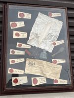 Full view of framed display showing multiple red wax seals on labeled paper pieces, two historic handwritten documents, iron quill pen, and small glass ink bottle.