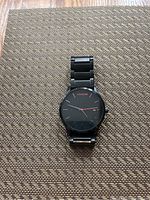Black MVMT wristwatch with a metal link strap shown on a textured surface.