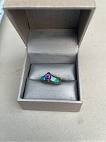 Ring with a central purple stone and two blue stones in a gray ring box